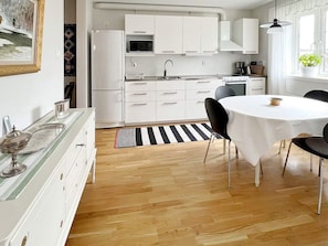 A modern kitchen with white cabinets, a microwave, and a stove. There is a dining table with chairs and a black and white striped rug.