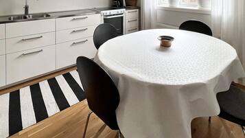 Una cocina moderna con armarios blancos, un lavamanos de acero inoxidable y una mesa redonda con mantel blanco.