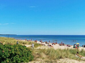 A beach with people sunbathing and swimming, surrounded by grass and bushes. - 6 Person Holiday Home in Yngsjo, Sverige (Yngsjo)