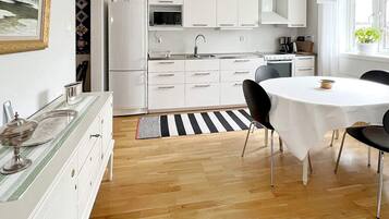 A modern kitchen with white cabinets, a microwave, and a stove. There is a dining area with a round table and chairs.