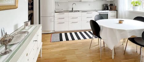 A modern kitchen with white cabinets, a microwave, and a stove. There is a dining area with a round table and chairs.