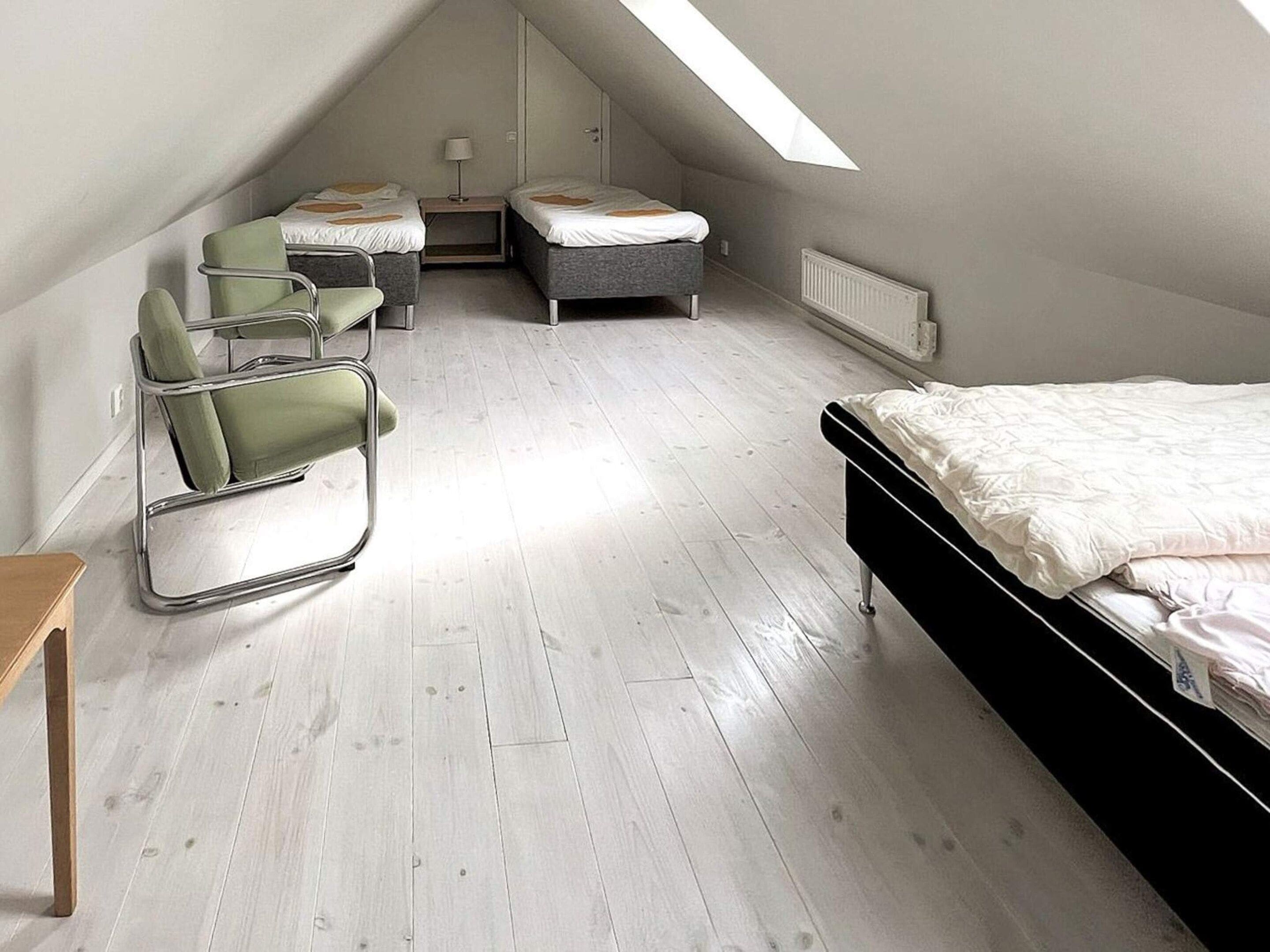 A room with a sloped ceiling, a bed, two chairs, a small table, and a radiator.