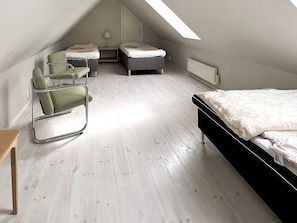 Una habitación con techo inclinado, una cama, dos sillas, una mesita y un radiador.