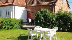 Une maison avec une porte rouge, une façade en briques et un mur extérieur blanc. On y trouve une petite terrasse avec une table et des chaises.