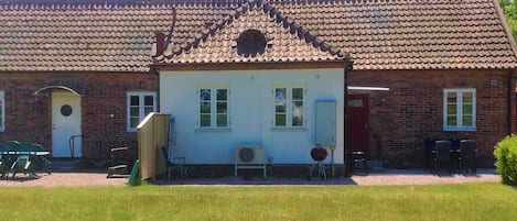 A two-story brick building with a tiled roof, a front door, and a small porch area with chairs.