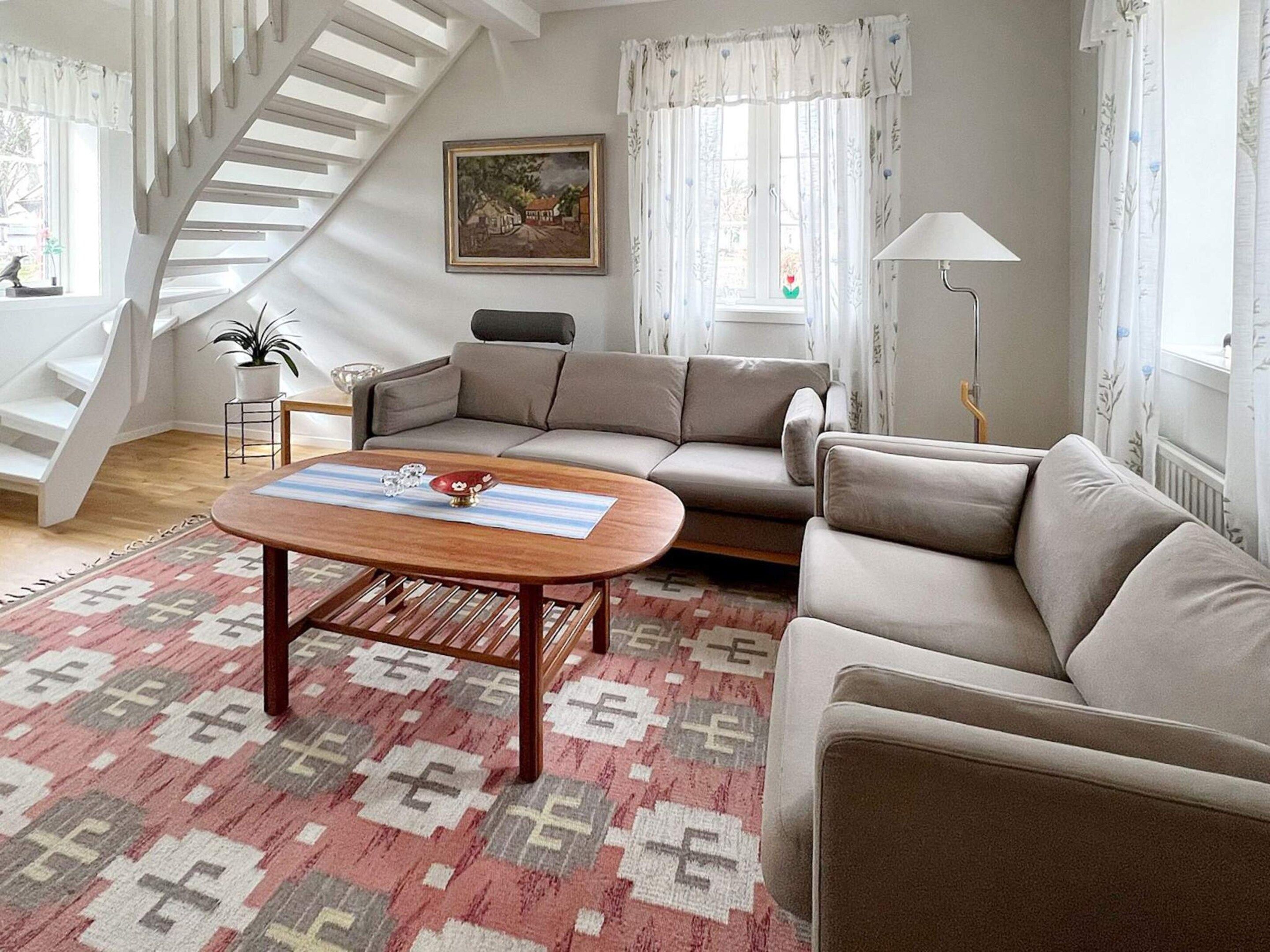 A living room with a sofa, a coffee table, a lamp, a staircase, and a painting on the wall.