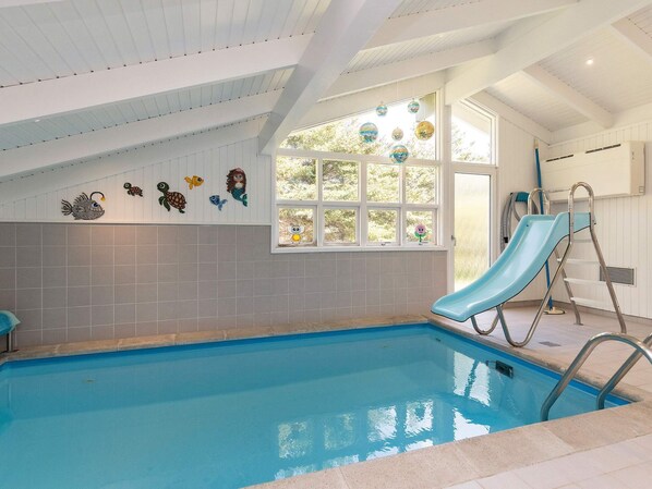 A swimming pool with a slide, a window with a view of trees, and a ceiling with white beams.