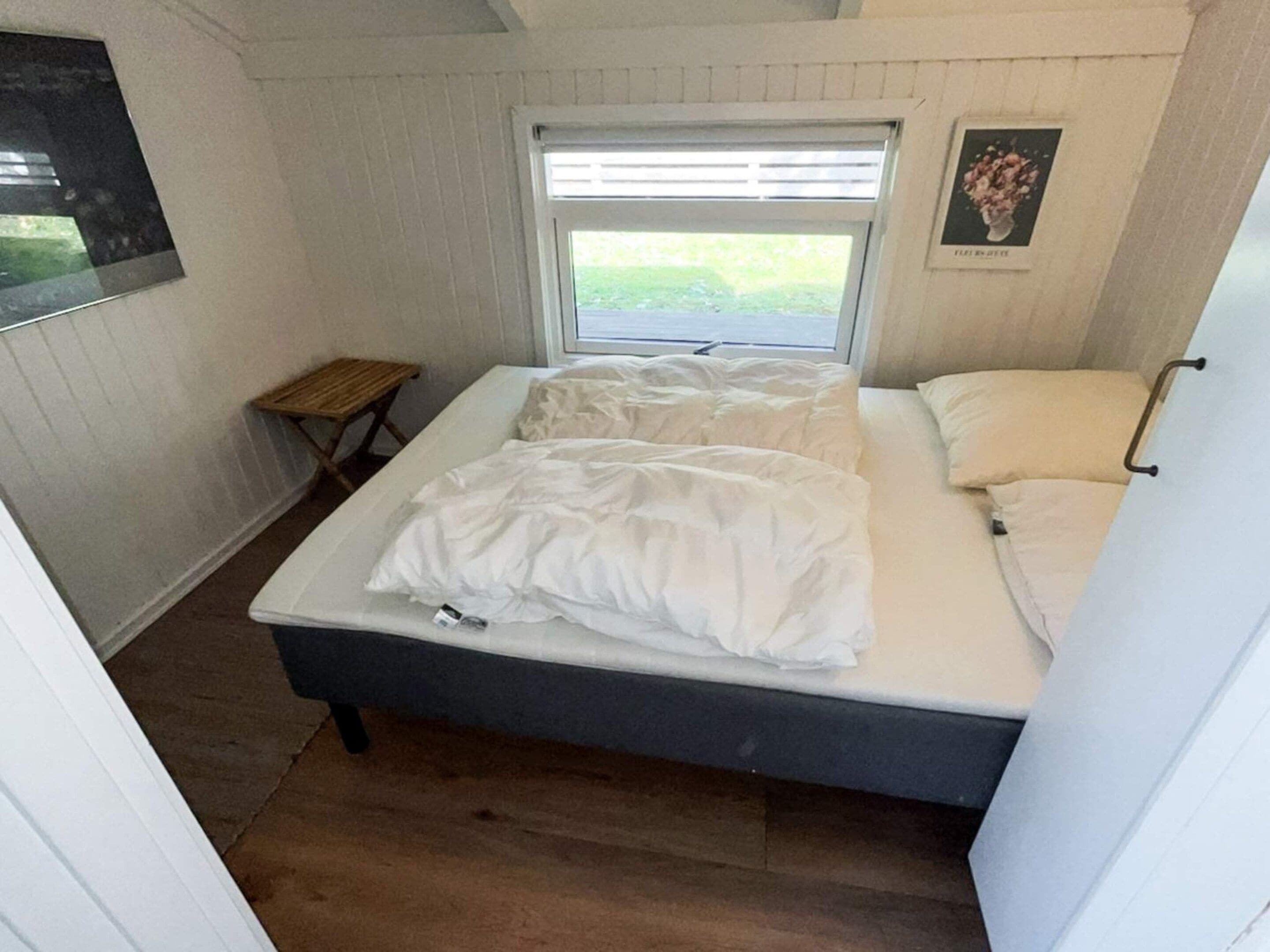 A single bed with white bedding in a room with white walls and a window.