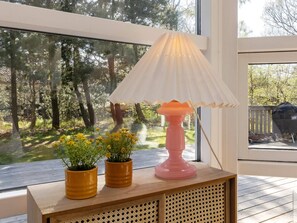 A room with a large window, a wooden table with a lamp, and two potted plants.