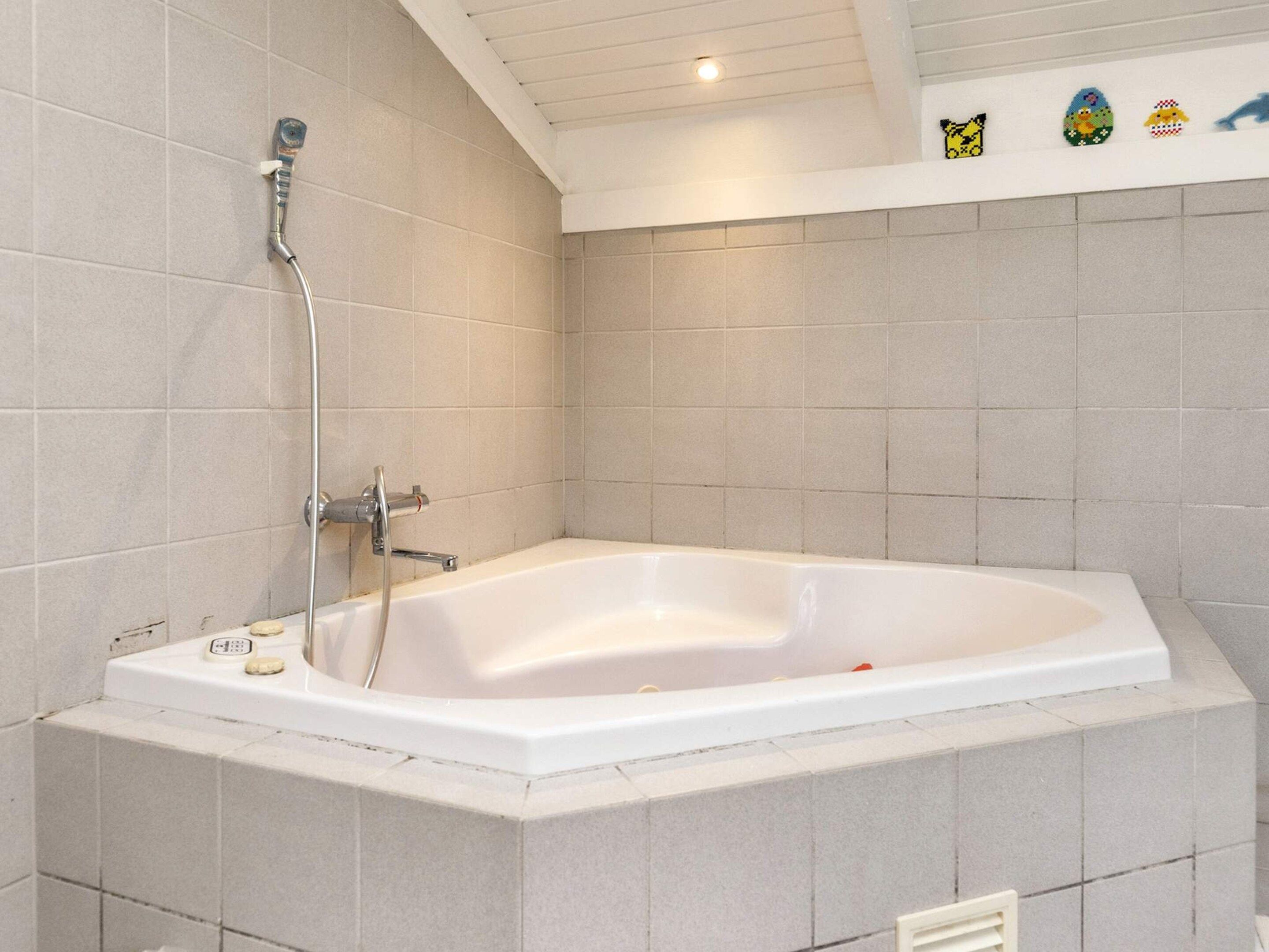 Une salle de bain avec une baignoire blanche, une pomme de douche et une étagère ornée d’objets décoratifs.