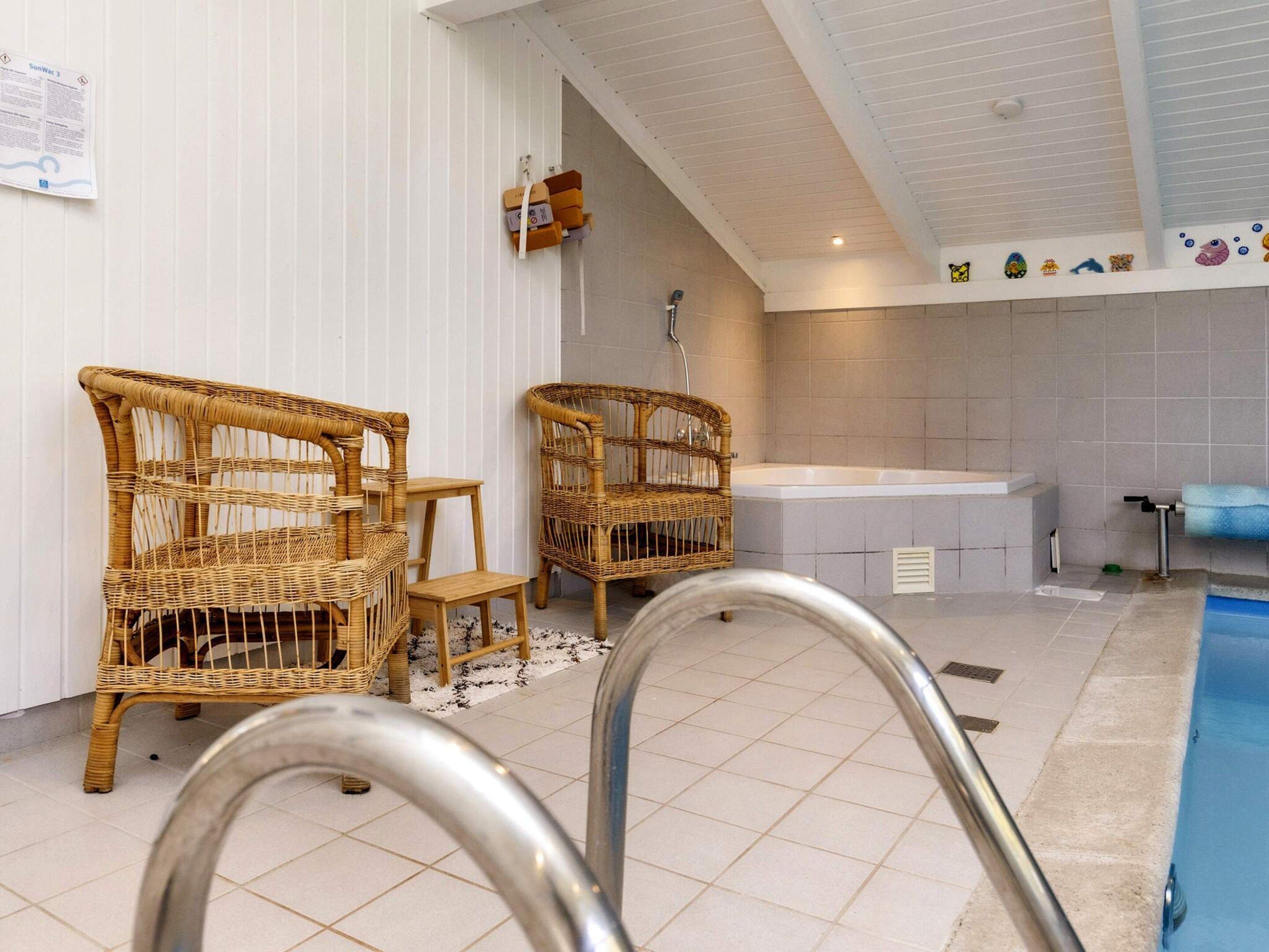 A bathroom with a bathtub, two wicker chairs, a small table, and a shower area.