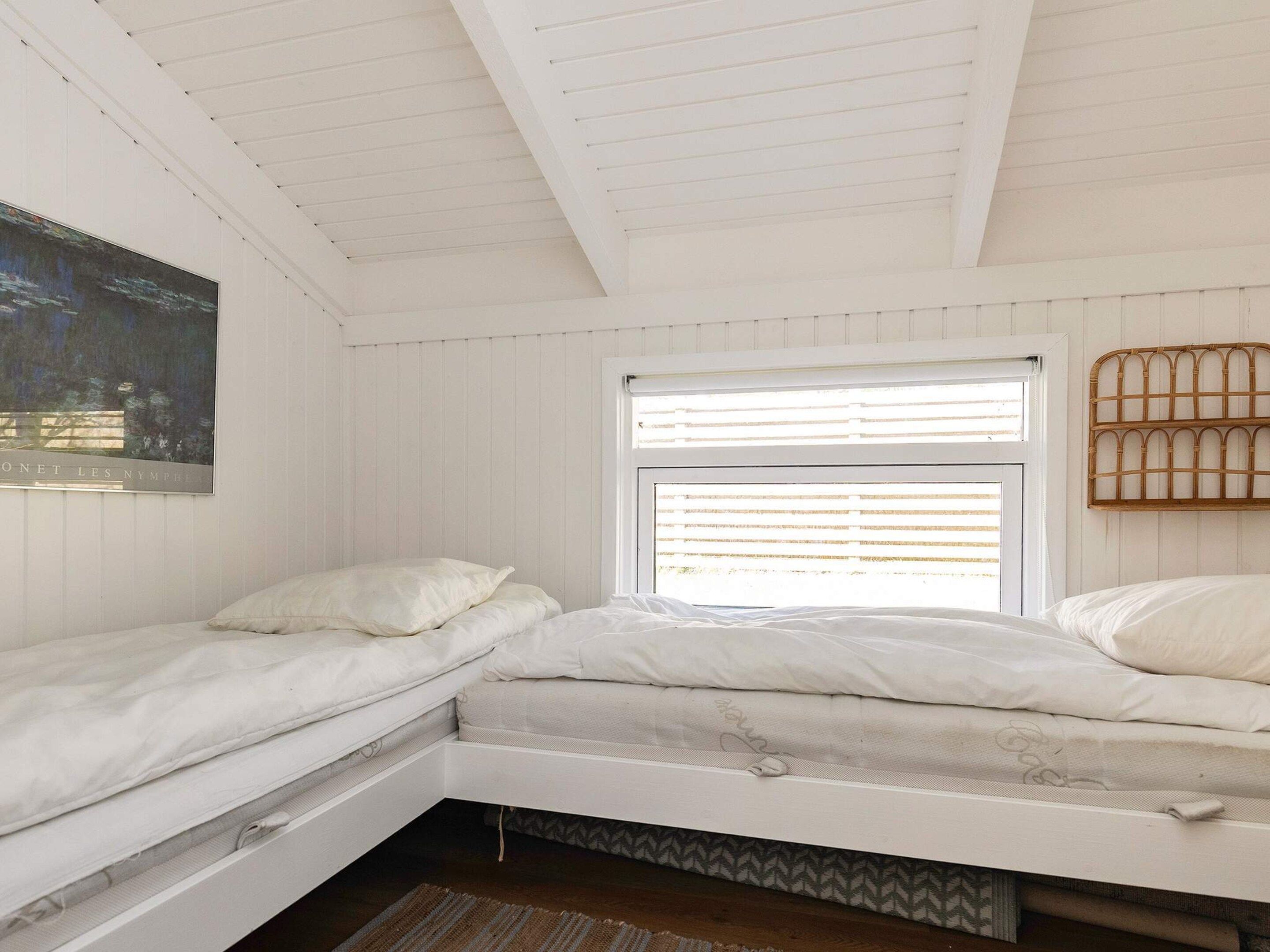 A bedroom with two beds, a window with blinds, a painting on the wall, and a woven headboard.
