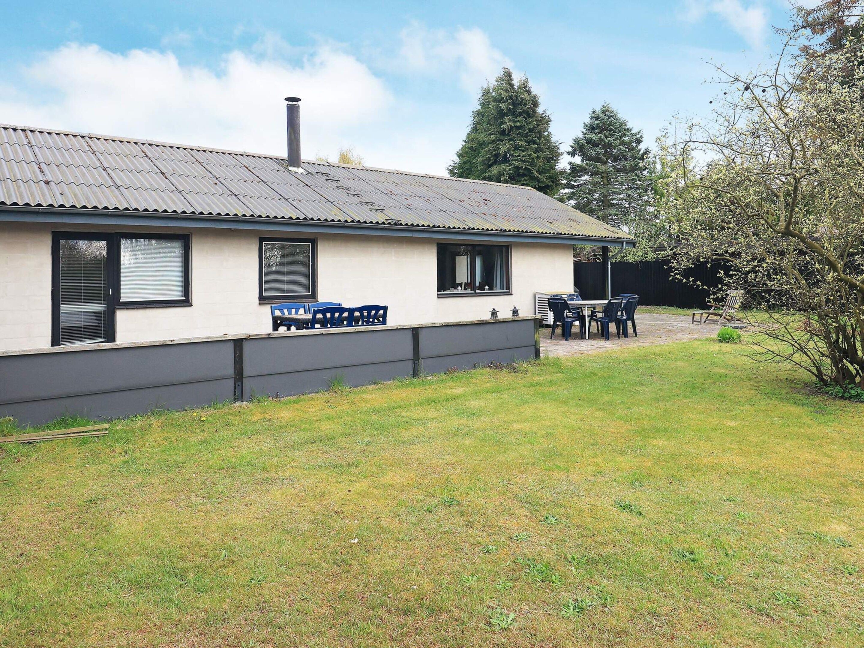 A single-story house with a metal roof, a chimney, and a small patio area with outdoor furniture.