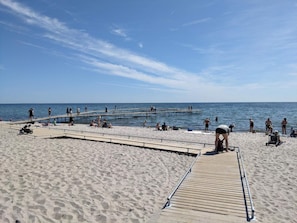 A beach with a wooden pier extending into the water, sandy beach, and clear skies. - 6 Person Holiday Home in Vaeggerlose (Vaeggerlose)