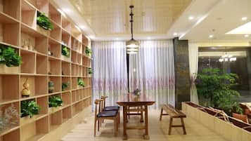 A room with a dining table, chairs, a bookshelf with plants, and a large window with curtains.
