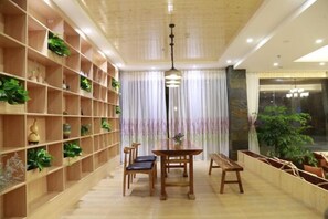 Une pièce comprenant une table à manger, des chaises, une bibliothèque avec des plantes et une grande fenêtre avec des rideaux.