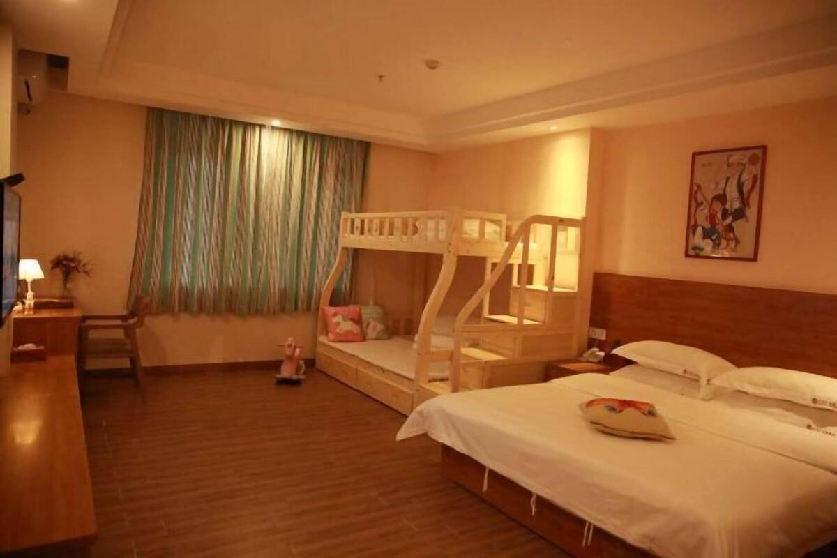 Habitación de hotel con literas, un escritorio, una silla, una mesita de noche y una ventana con cortinas.
