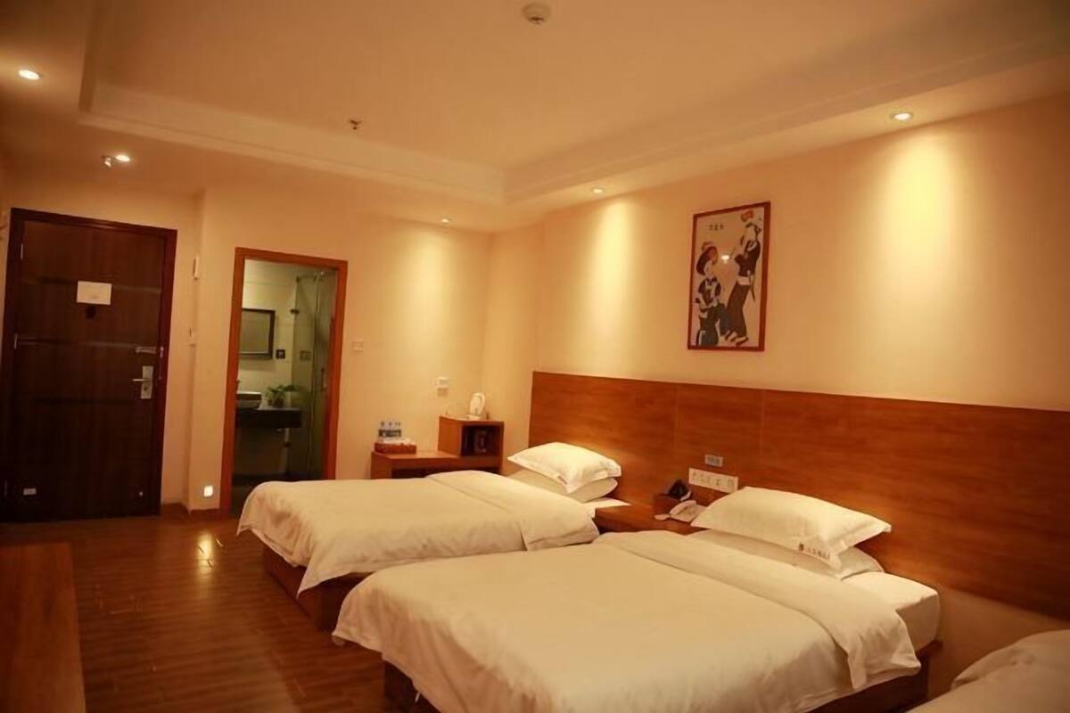 Habitación de hotel con dos camas, piso de madera, cabecero de madera, un cuadro en la pared y una puerta que da al baño.