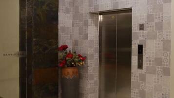 Un ascensor con un panel de control digital, una planta en maceta con flores rojas y una pared con azulejos de diseño geométrico.