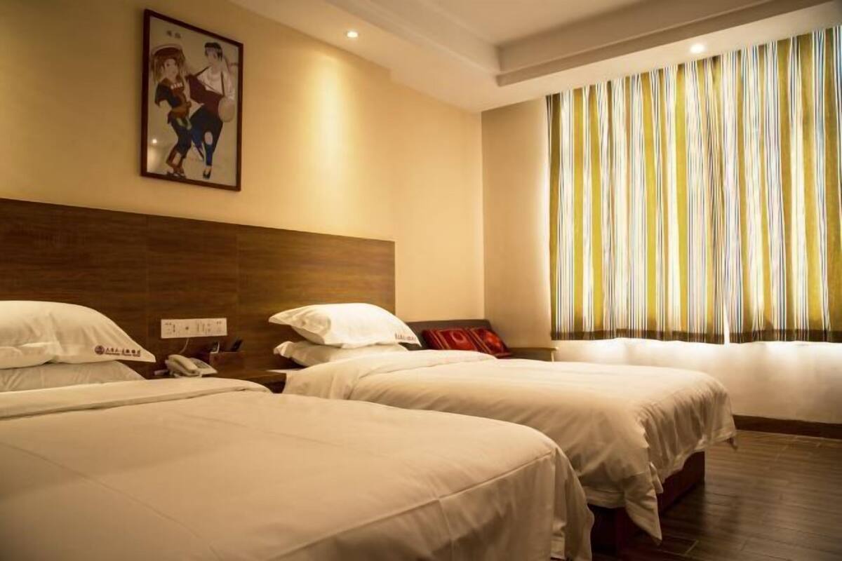 Habitación de hotel con dos camas, cabecera de madera, un cuadro en la pared, un teléfono y una ventana con cortinas a rayas.