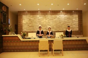 A reception desk with three staff members, a clock, and a decorative wall. - Sanyuesan Theme Hotel (Liannan)