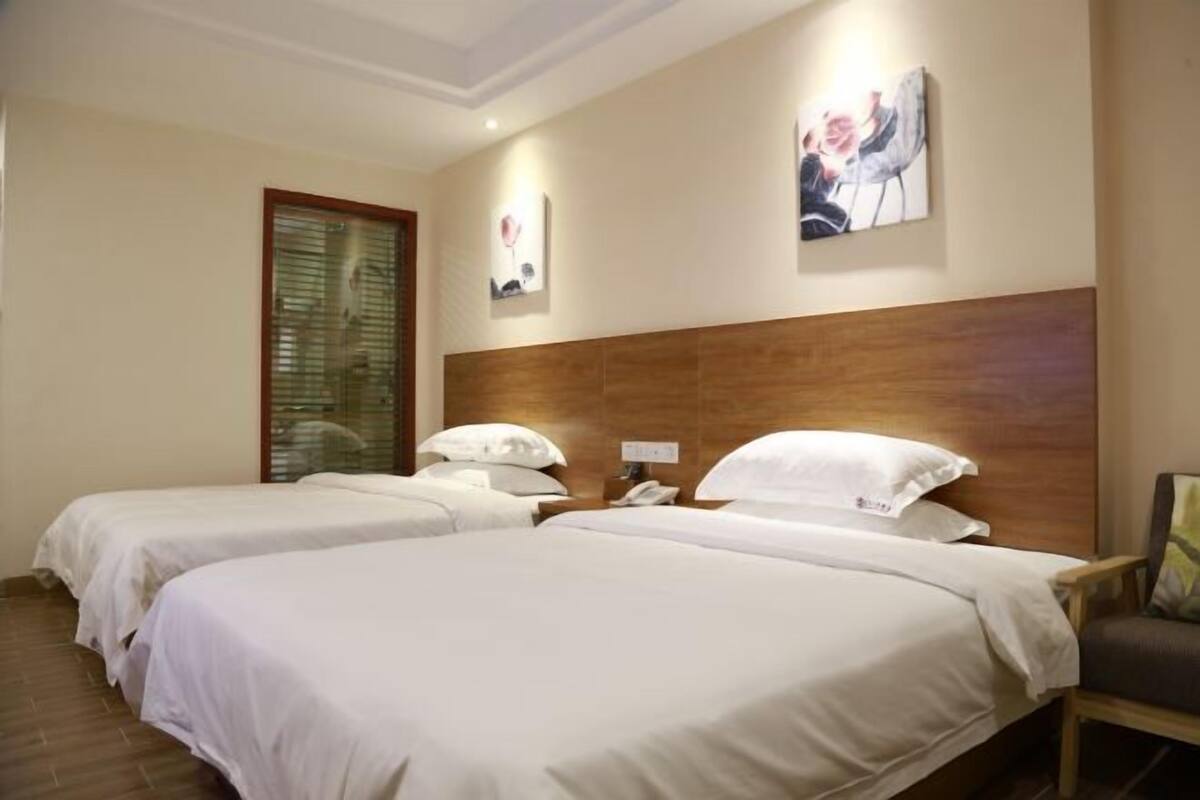 Habitación de hotel con dos camas, cabecero de madera, una mesita de noche con teléfono y obras de arte en las paredes.