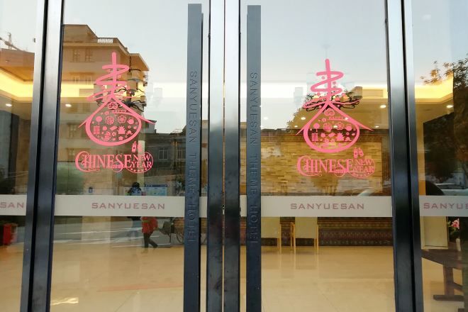 Entrada de hotel con puerta de vidrio que muestra el nombre y el logo del hotel en rosa.