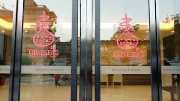 Entrada de hotel con puerta de vidrio que muestra el nombre y el logo del hotel en rosa.
