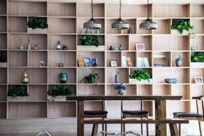 A room with a wooden bookshelf filled with plants and books, a wooden dining table with chairs, and pendant lights. - Sanyuesan Theme Hotel (Liannan)