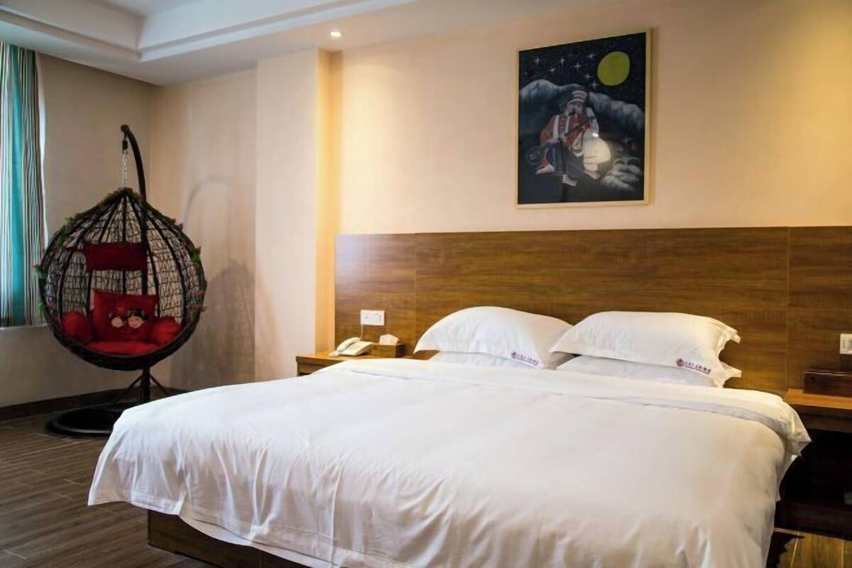 Habitación de hotel con una cama grande, un sillón colgante, cabecera de madera, pintura de cielo nocturno y una mesita de noche con un teléfono.