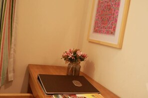 A laptop on a wooden desk with a vase of flowers, a framed picture on the wall, and a window with curtains. - Sanyuesan Theme Hotel (Liannan)