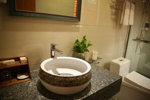Un baño con un lavabo redondo, un espejo, una planta y un inodoro.
