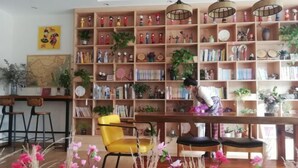 Una habitación acogedora con una estantería de madera llena de libros y adornos, un sillón amarillo y una mesa de comedor de madera.
