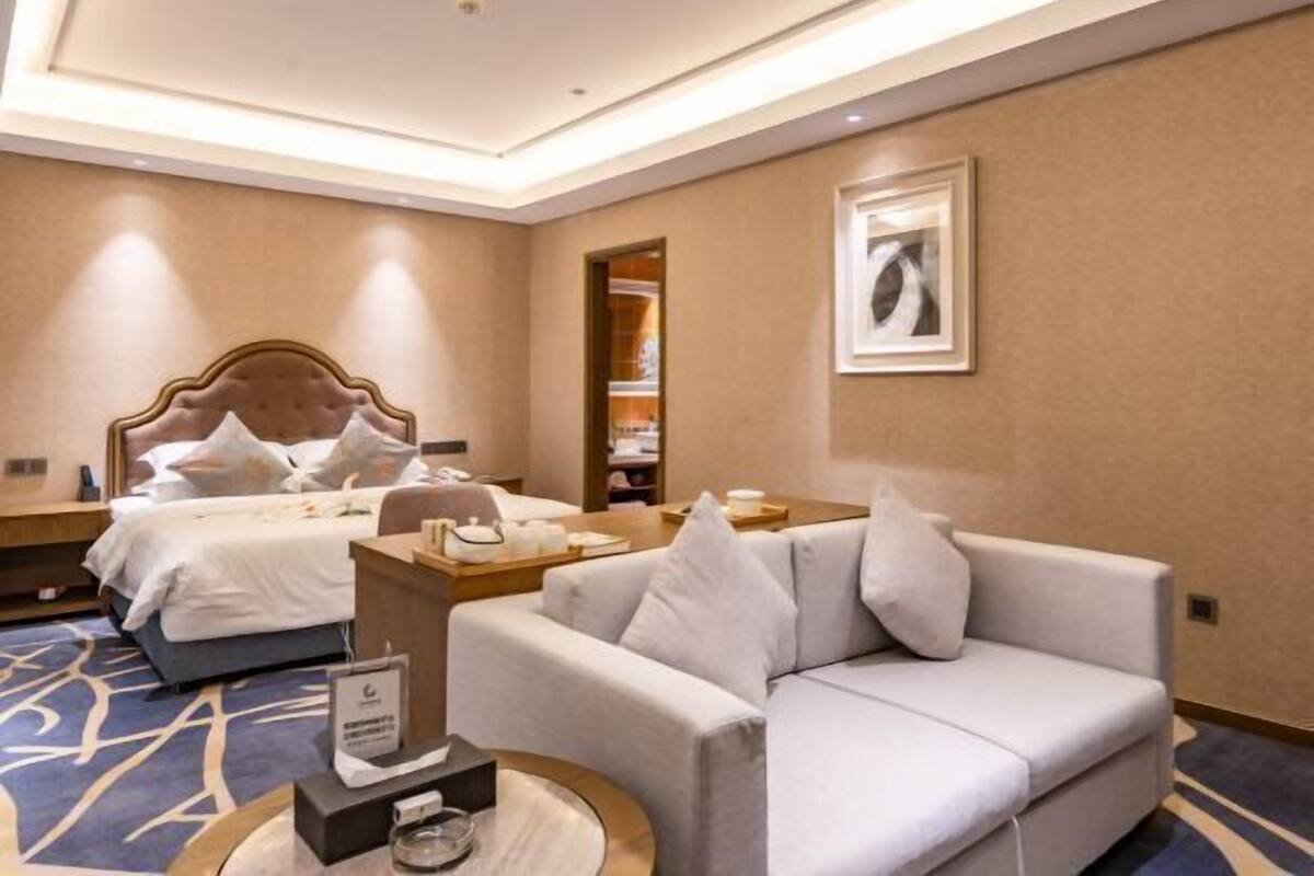 A hotel room with a bed, a sofa, a coffee table, and a framed picture on the wall.