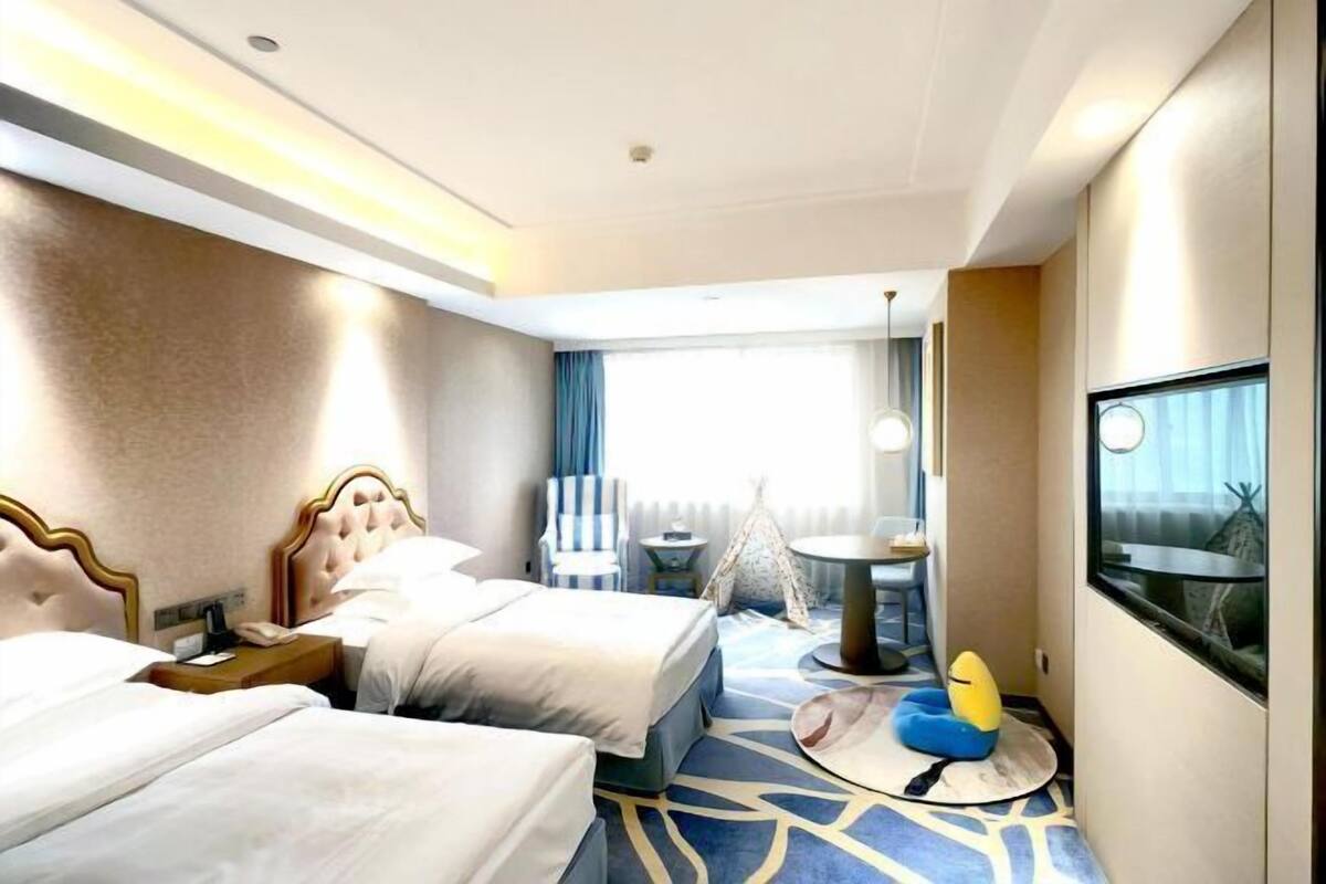 A hotel room with two beds, a small table, a chair, a round seating area, and a television.