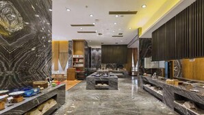 Um hall de hotel moderno com piso de mármore, uma área de estar central e um balcão de recepção.