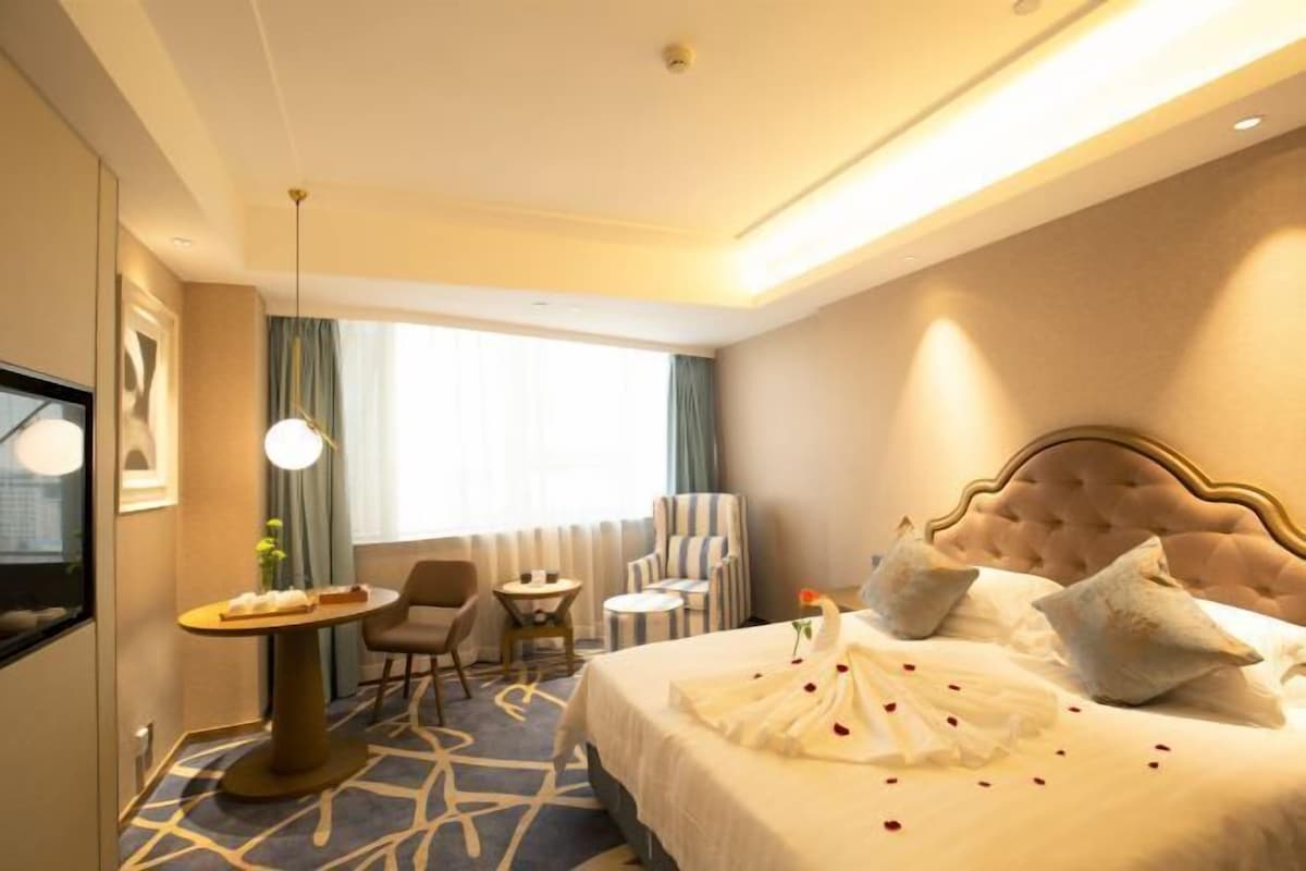 A hotel room with a large bed, a desk, a chair, and a TV.