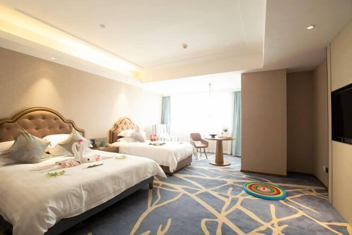 A hotel room with two beds, a small table, a chair, and a TV.