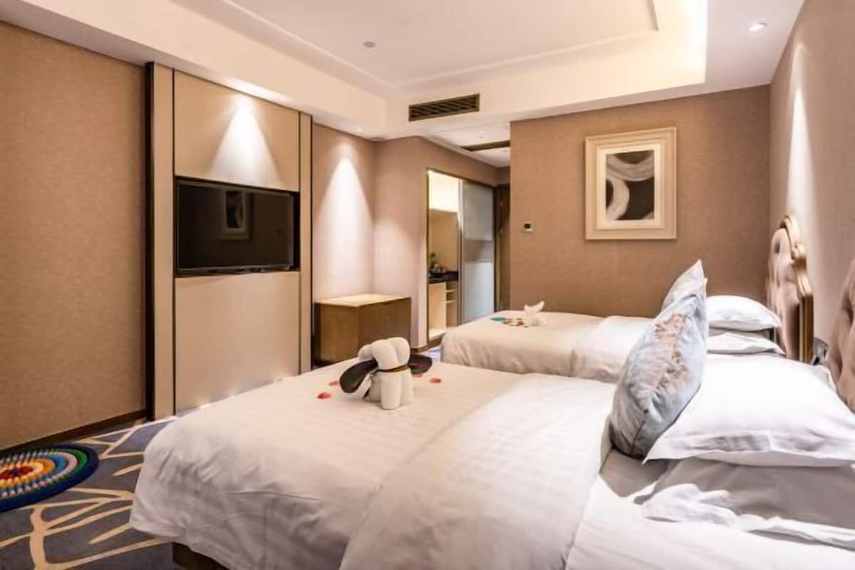 A hotel room with two beds, a TV, a minibar, and a large mirror.