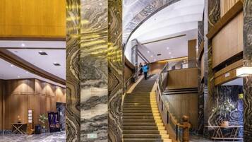A grand staircase with marble columns, a reception area with wooden paneling, and a curved ceiling.