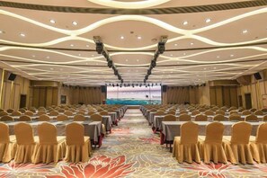 A conference room with rows of tables and chairs, a large screen at the front, and a patterned carpet. - Sunny Hotel (Taizhou)