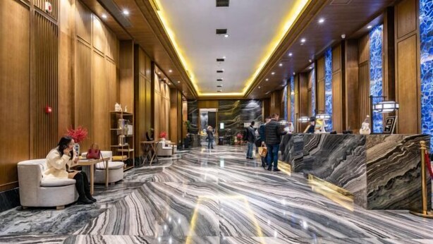 Um hall de hotel com piso de mármore, painéis de madeira e uma mesa de recepção.