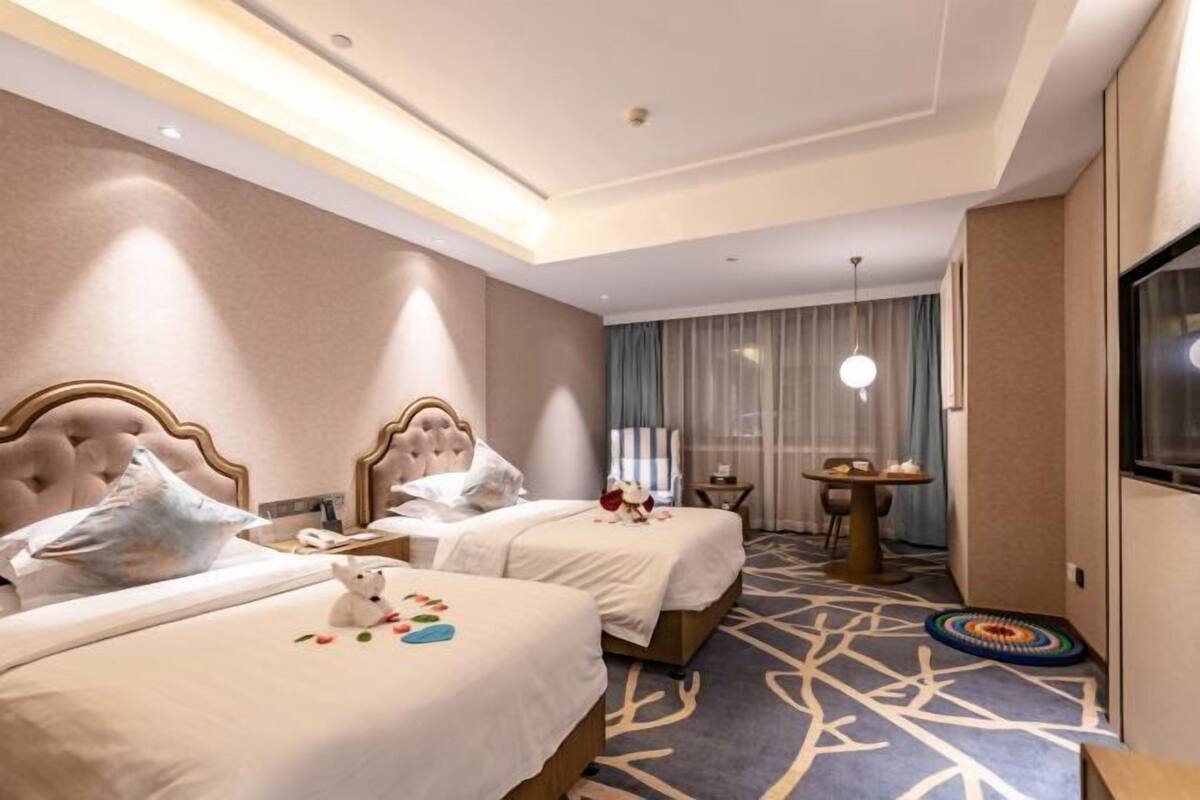 A hotel room with two beds, a small table, a chair, a TV, and a patterned carpet.