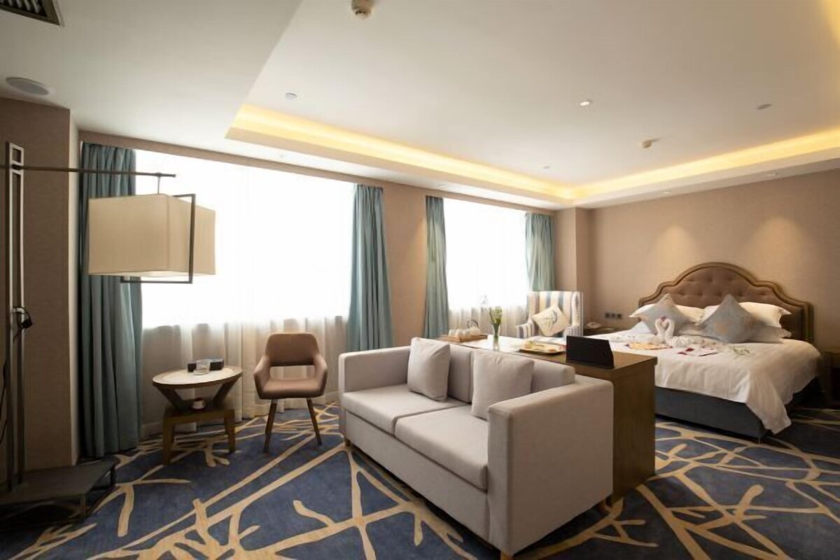 A hotel room with a bed, a sofa, a desk, and a lamp.