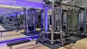 Uma academia com diversos aparelhos de exercício, um banco e espelhos nas paredes.