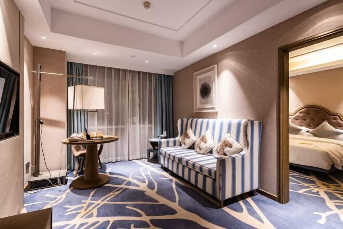 A hotel room with a striped sofa, a round table, a bed with a tufted headboard, and a large mirror.