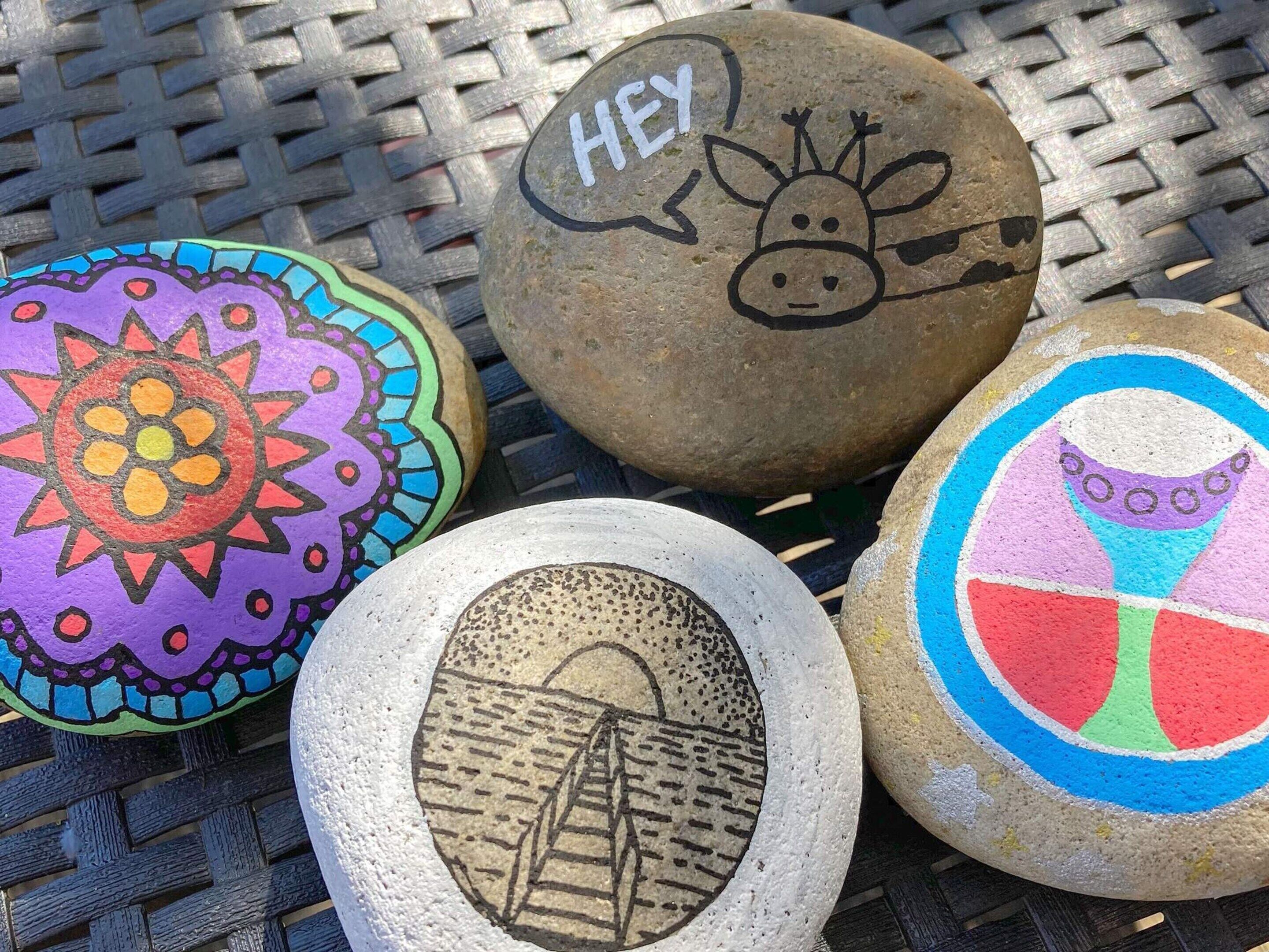 Four painted rocks with various designs, including a sun, a cow, a bridge, and a colorful geometric pattern.