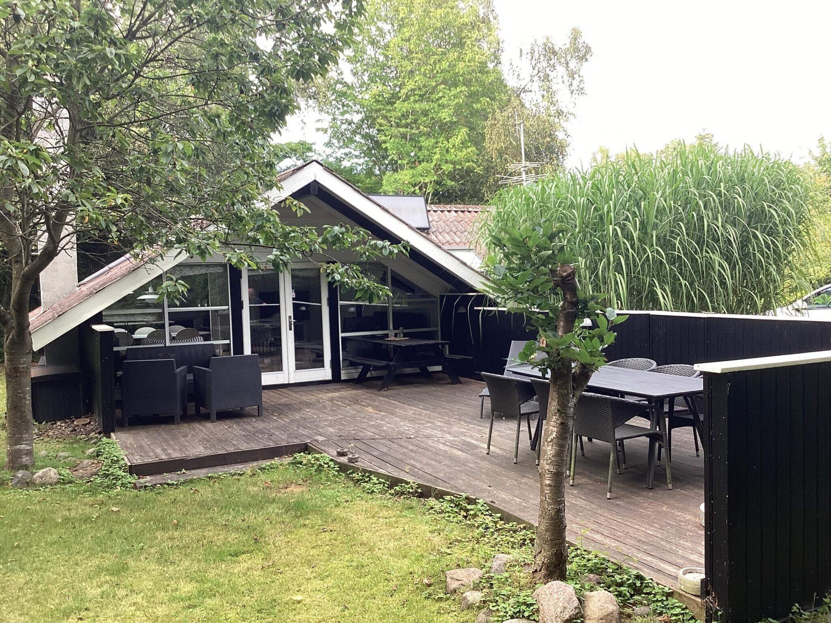 A covered patio with outdoor furniture, a wooden deck, and a view of the surrounding greenery.
