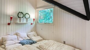 A bedroom with a sloped ceiling, a bed with white bedding, two wall-mounted sconces, and a window with a view of greenery. - 6 Person Holiday Home in Vaeggerlose (Vaeggerlose)