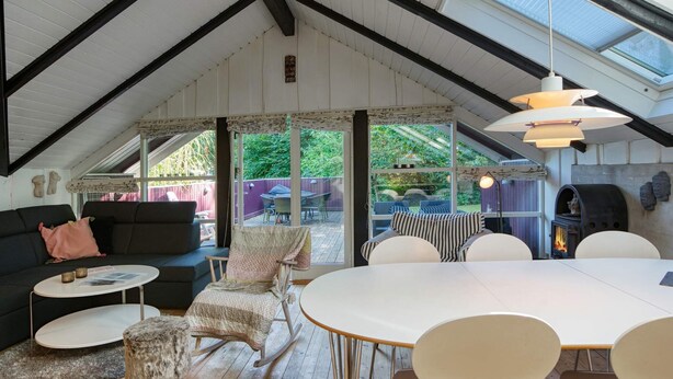 A cozy, well-lit attic room with a high ceiling, a dining table, chairs, a sofa, and a fireplace. - 6 Person Holiday Home in Vaeggerlose (Vaeggerlose)